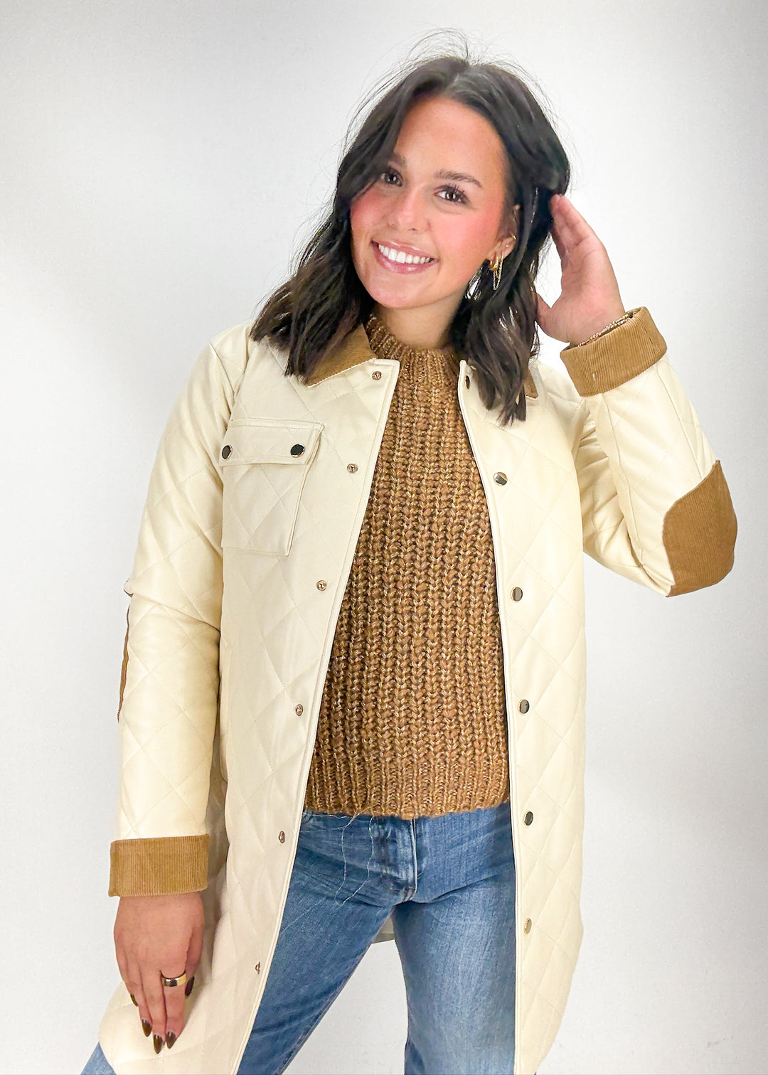 Woman wearing a cream jacket over a brown sweater and blue jeans 