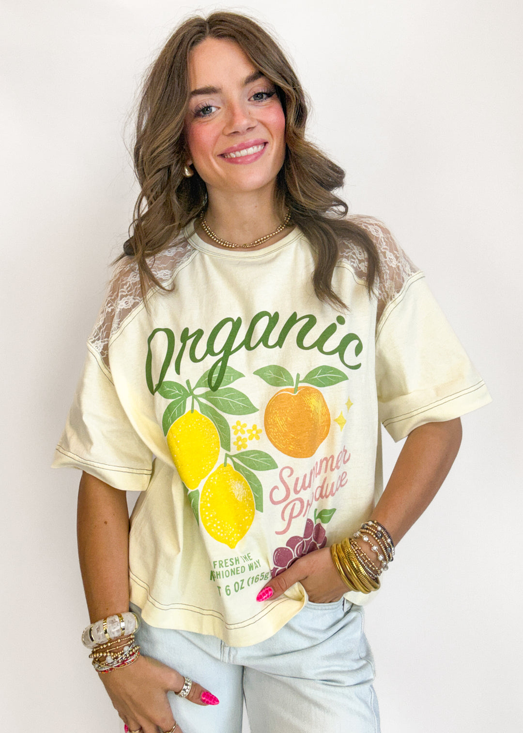 Woman wearing a cream-colored t-shirt with graphics and text, standing against a plain background.