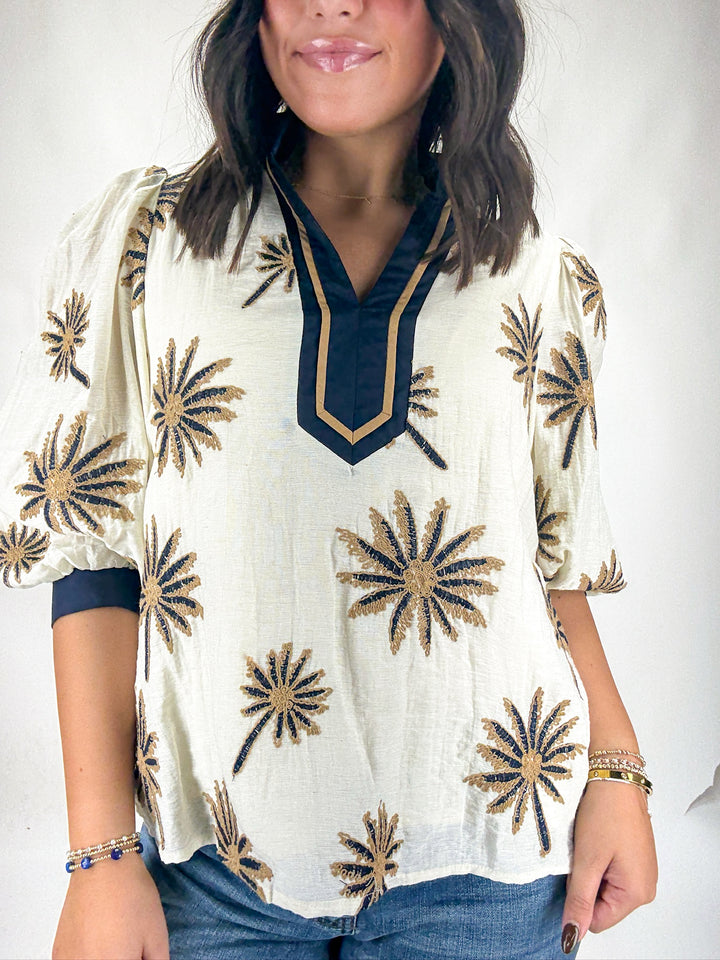 Woman wearing a white blouse with gold floral patterns on a plain background