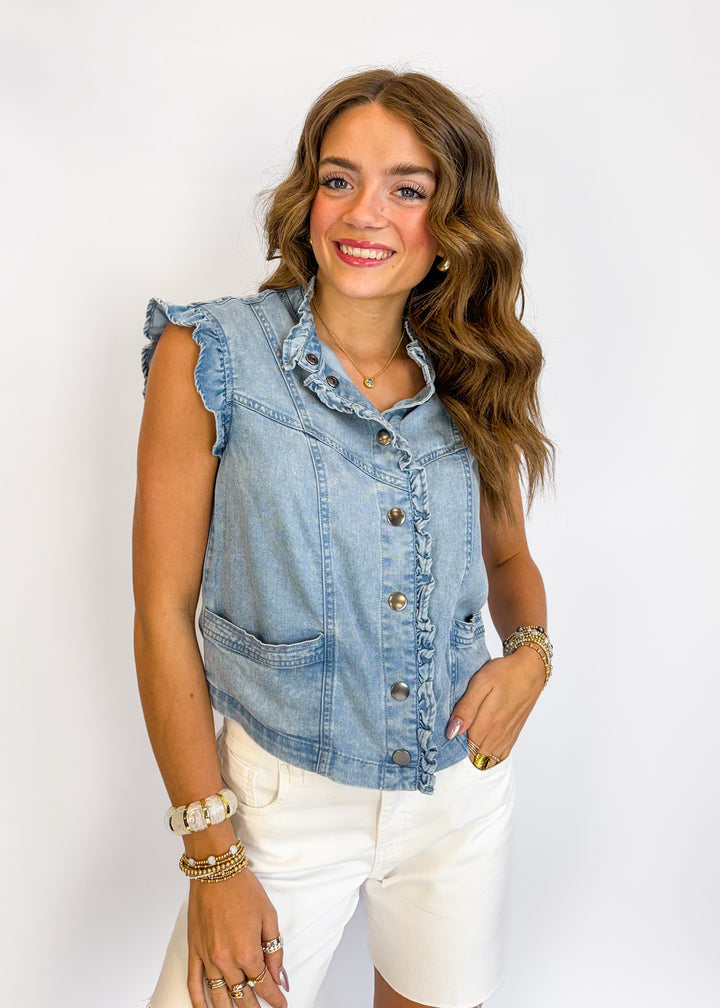 Woman wearing a denim vest over a white top on a plain background