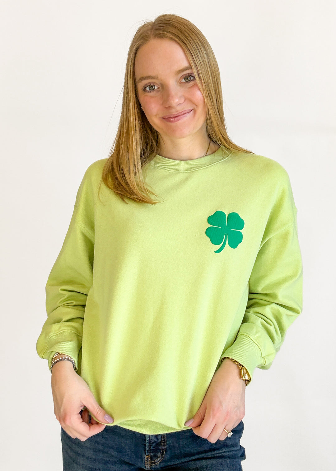 Woman wearing a light green sweatshirt with a four-leaf clover design on a plain background