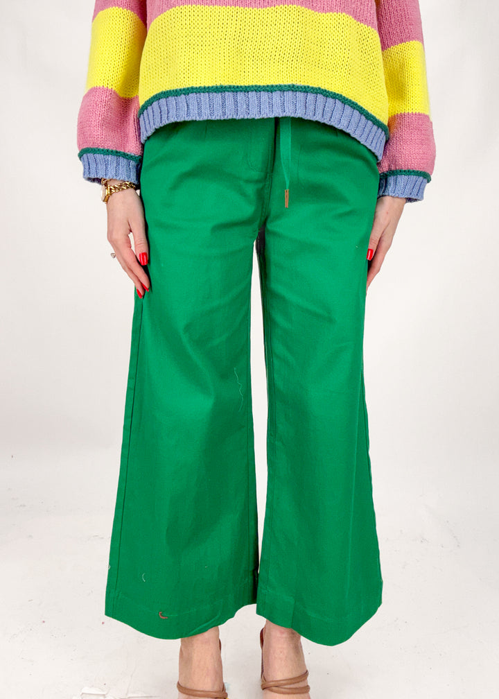 Person wearing a colorful sweater and green pants on a white background