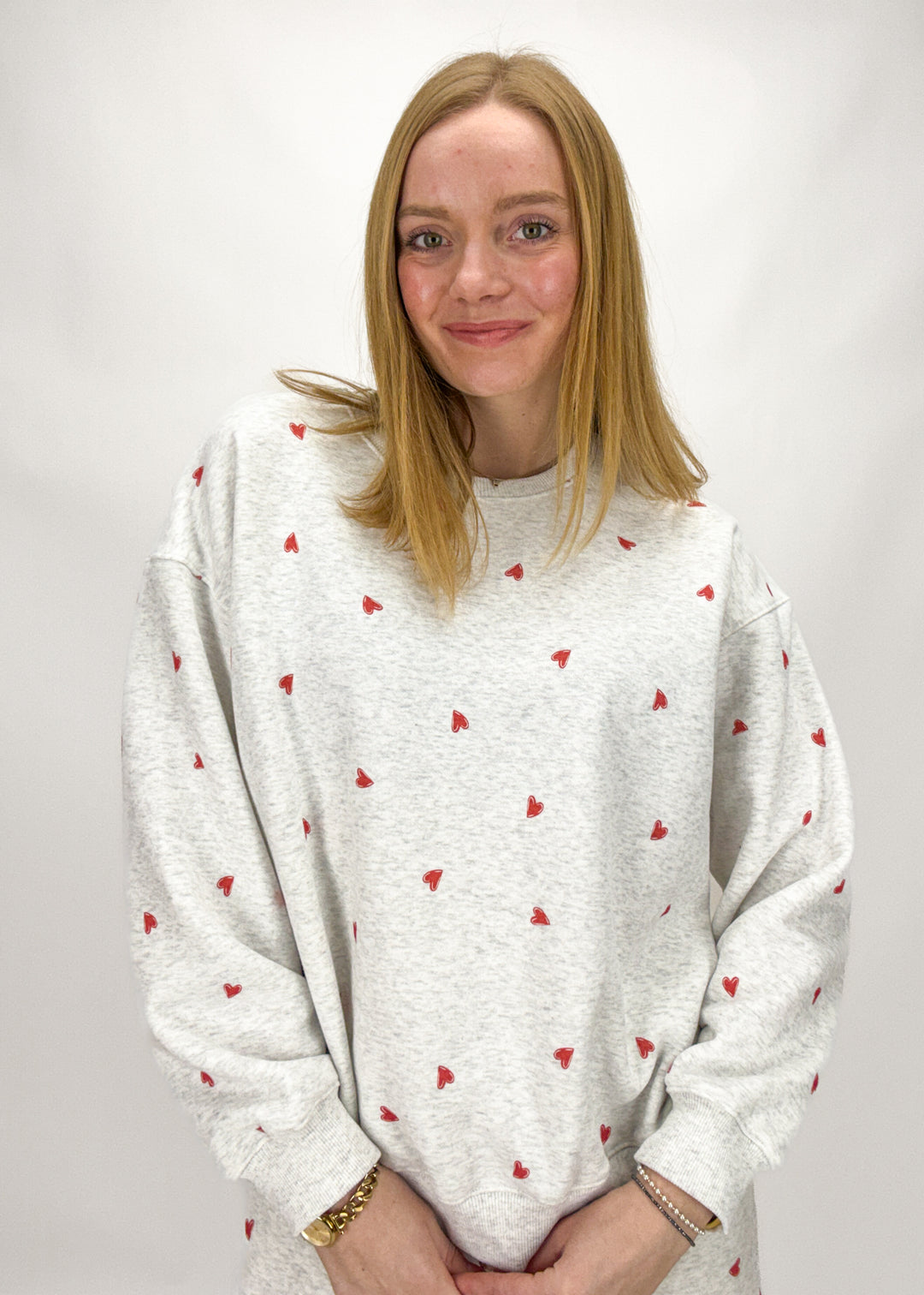 Person wearing a white sweater with red heart patterns on a plain background