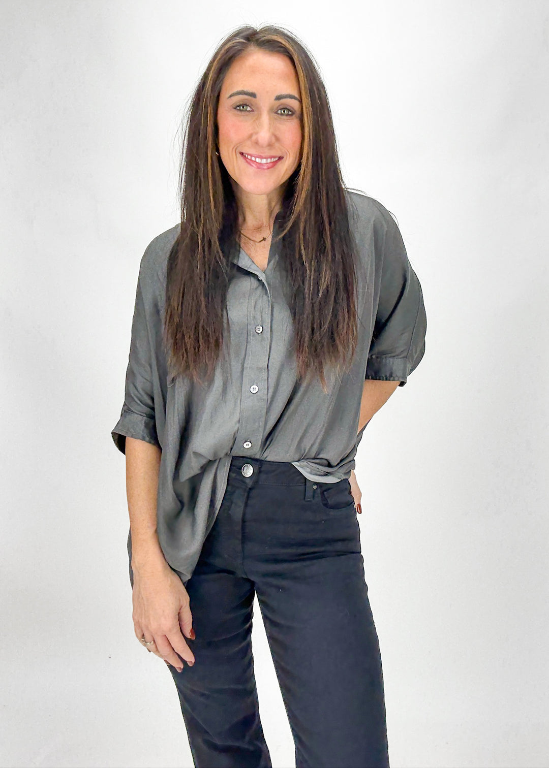 Woman wearing a gray shirt and dark pants against a white background