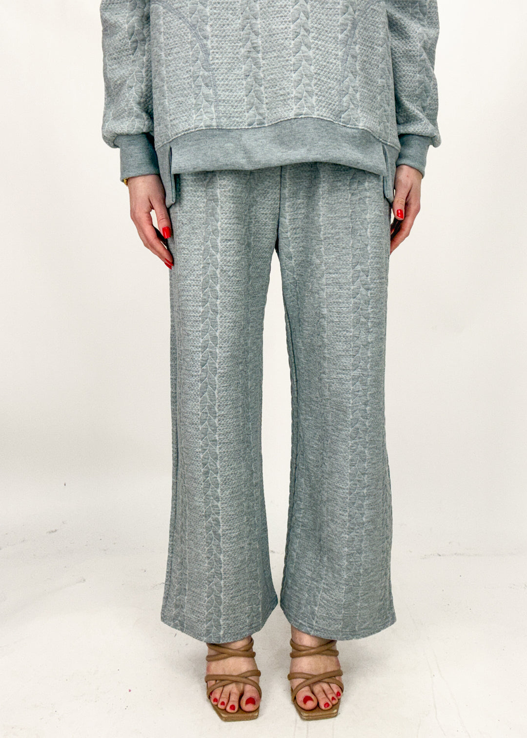 Person wearing a gray textured sweater and wide-leg pants on a white background