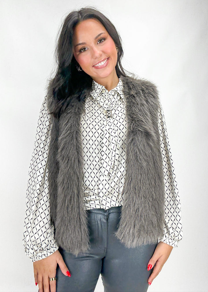 Woman wearing a gray fur vest over a patterned shirt with a white background