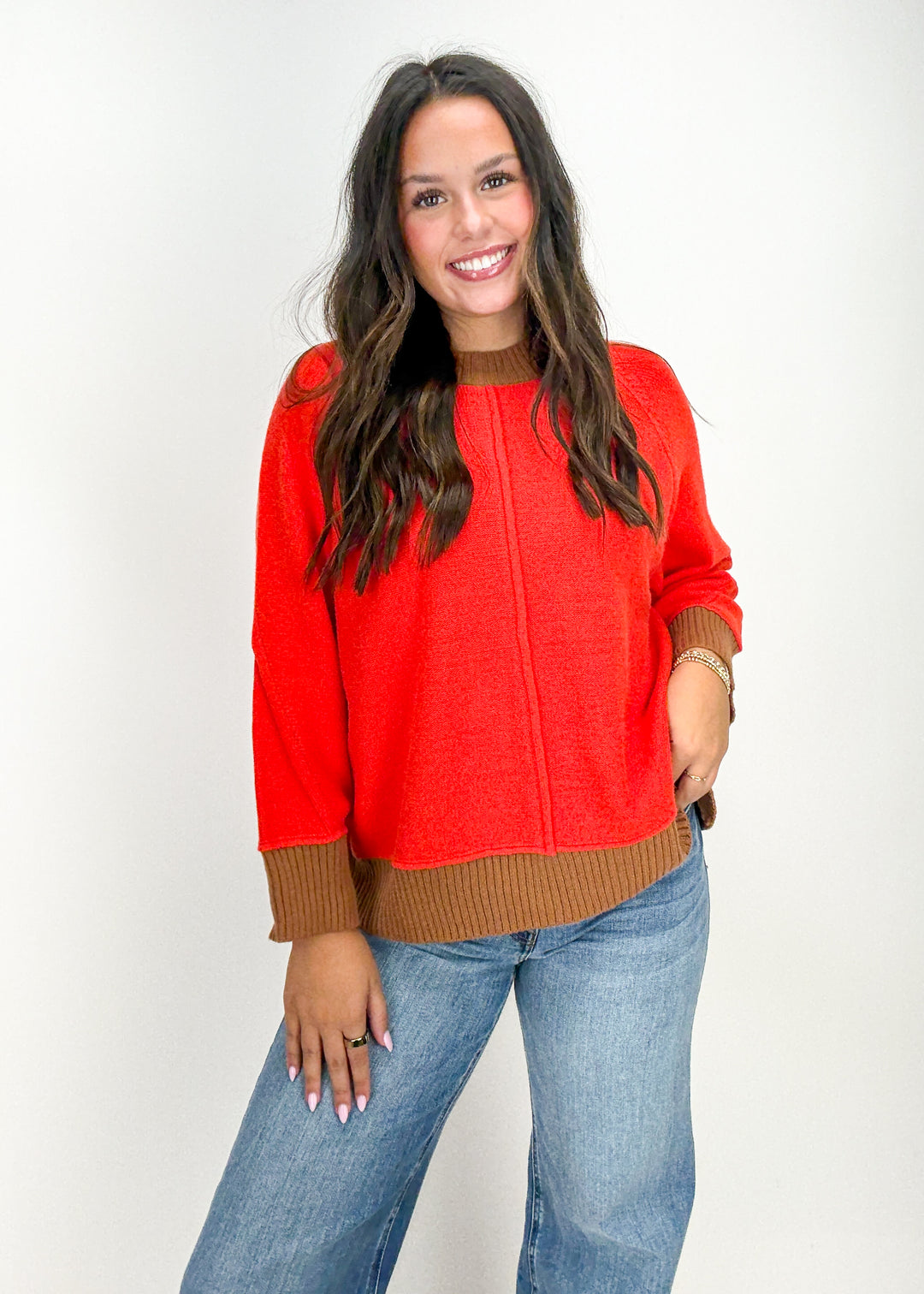 Woman wearing a red sweater with brown trim and blue jeans 