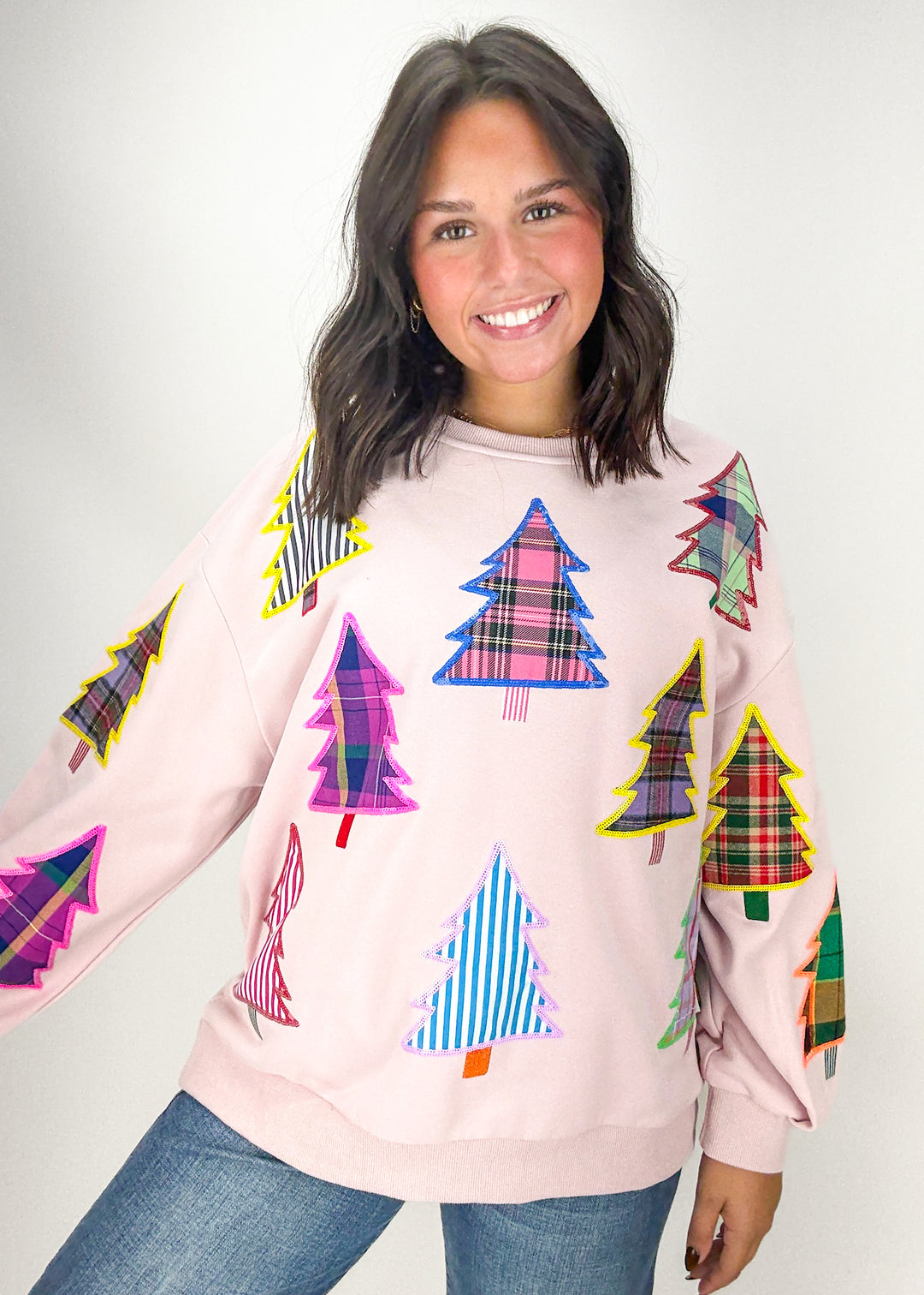 Woman wearing a pink sweater with colorful plaid tree patterns 
