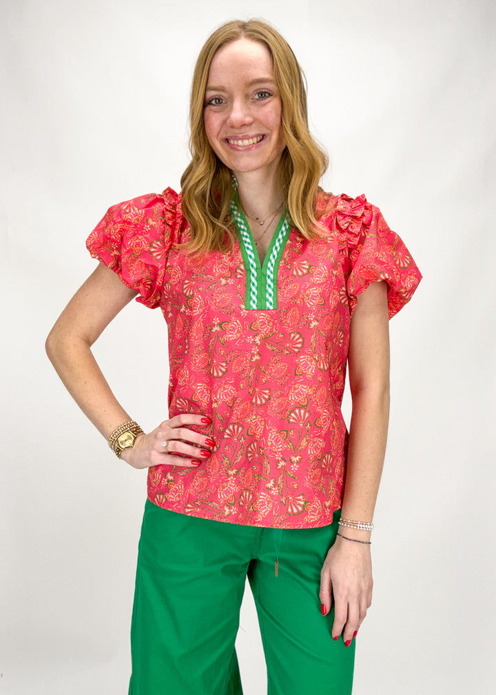 Woman wearing a pink floral blouse and green pants on a white background