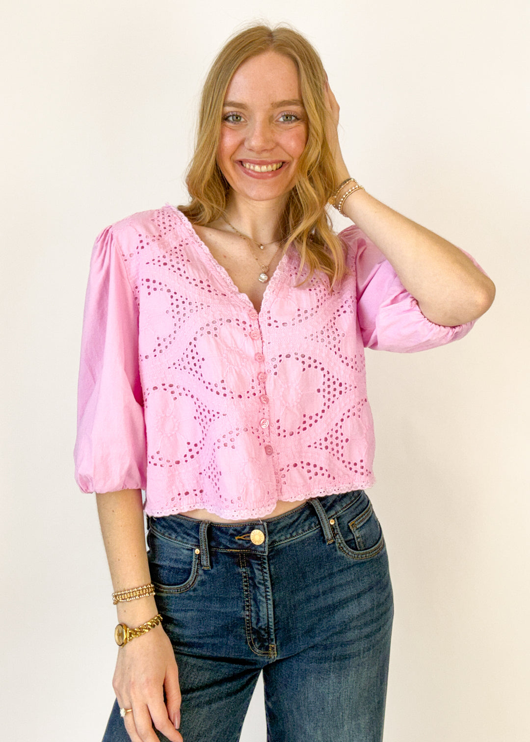 Woman wearing a pink blouse with cut-out details and blue jeans on a plain background