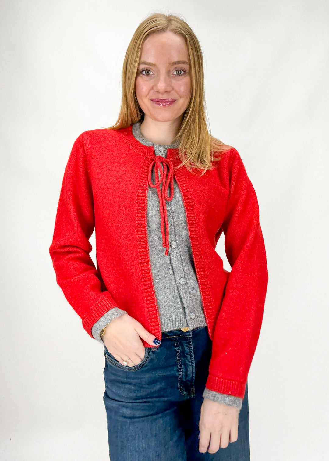 Woman wearing a red cardigan over a gray sweater with a white background