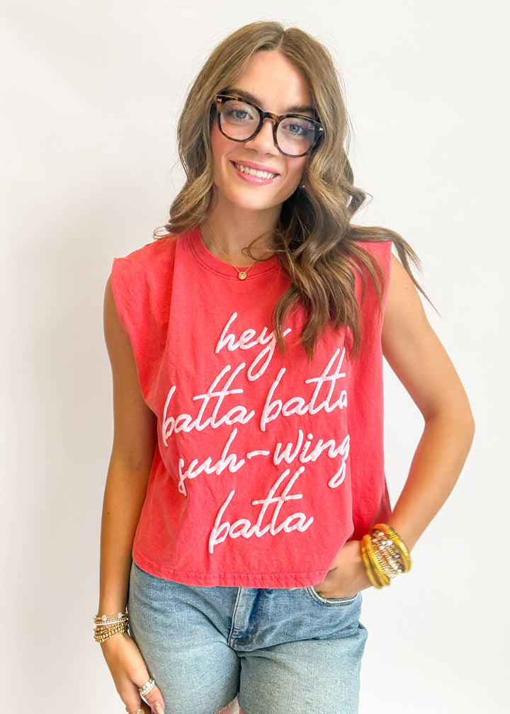Woman wearing a red sleeveless shirt with text, standing against a plain background