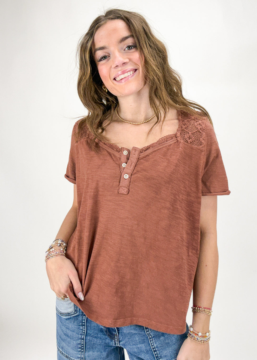 Woman wearing a brown short-sleeve top with lace details on a white background
