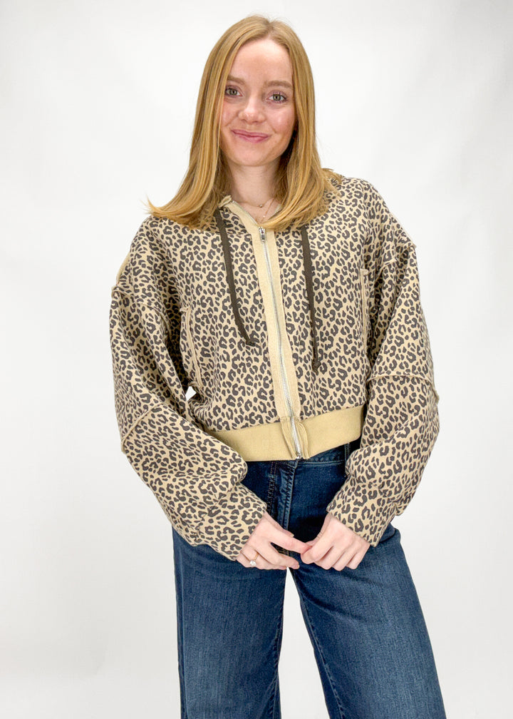 Person wearing a leopard print hoodie with a beige zipper on a white background