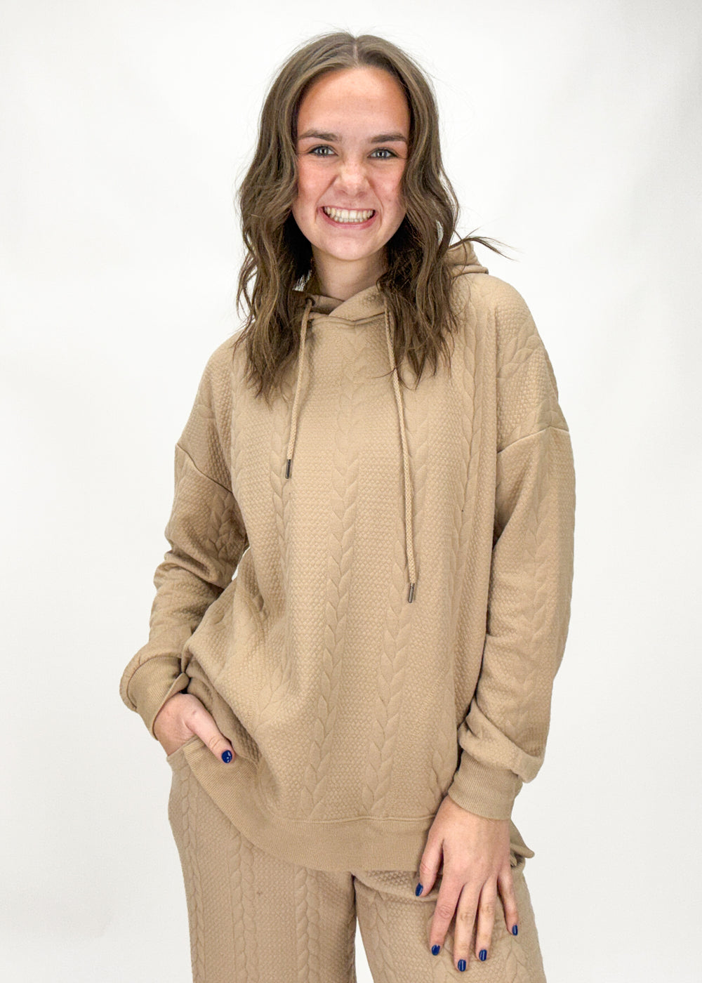 Woman wearing a beige cable knit hoodie and pants on a white background