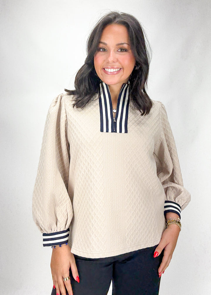 Woman wearing a beige long-sleeve top with striped cuffs and collar against a white background