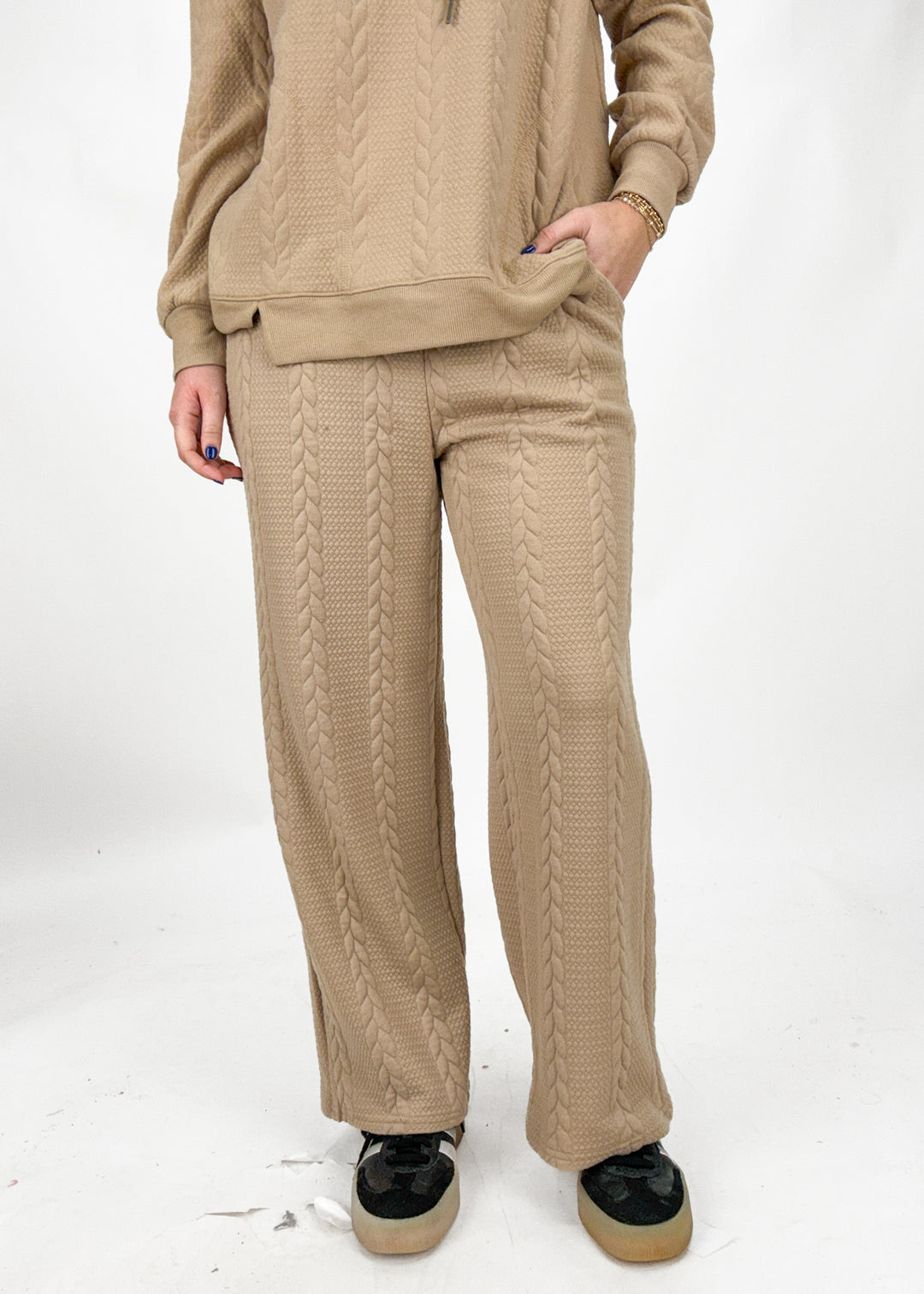 Person wearing a beige cable knit outfit on a white background