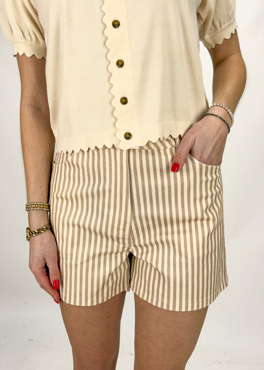 Person wearing a beige top with ruffled details and striped shorts on a white background