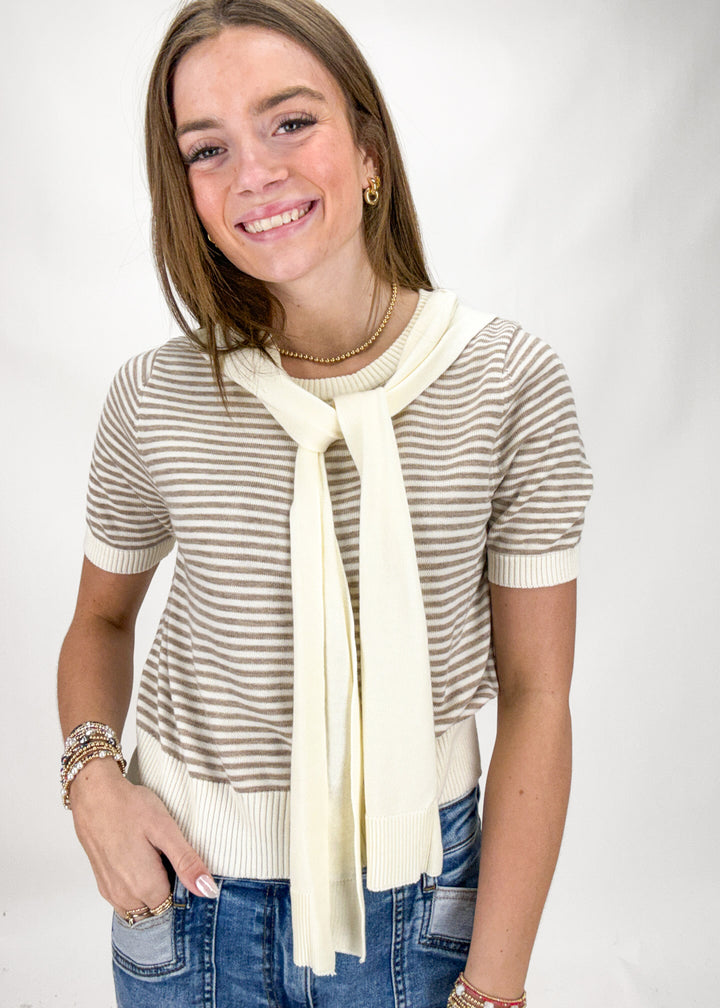 Woman wearing a striped sweater with a long cream scarf against a white background