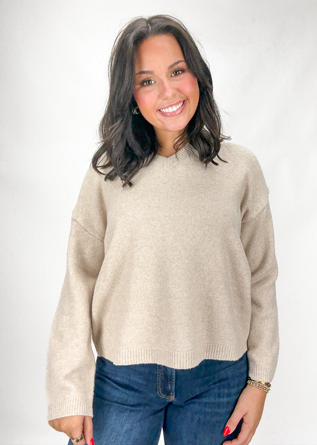 Woman wearing a beige sweater and blue jeans on a white background
