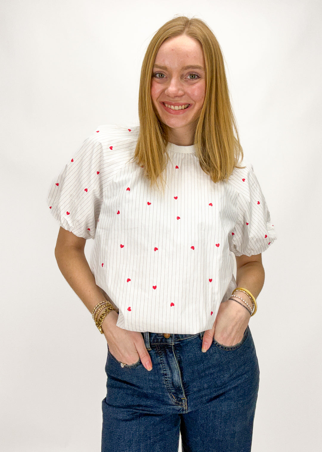 Woman wearing a white blouse with red patterns and blue jeans on a white background