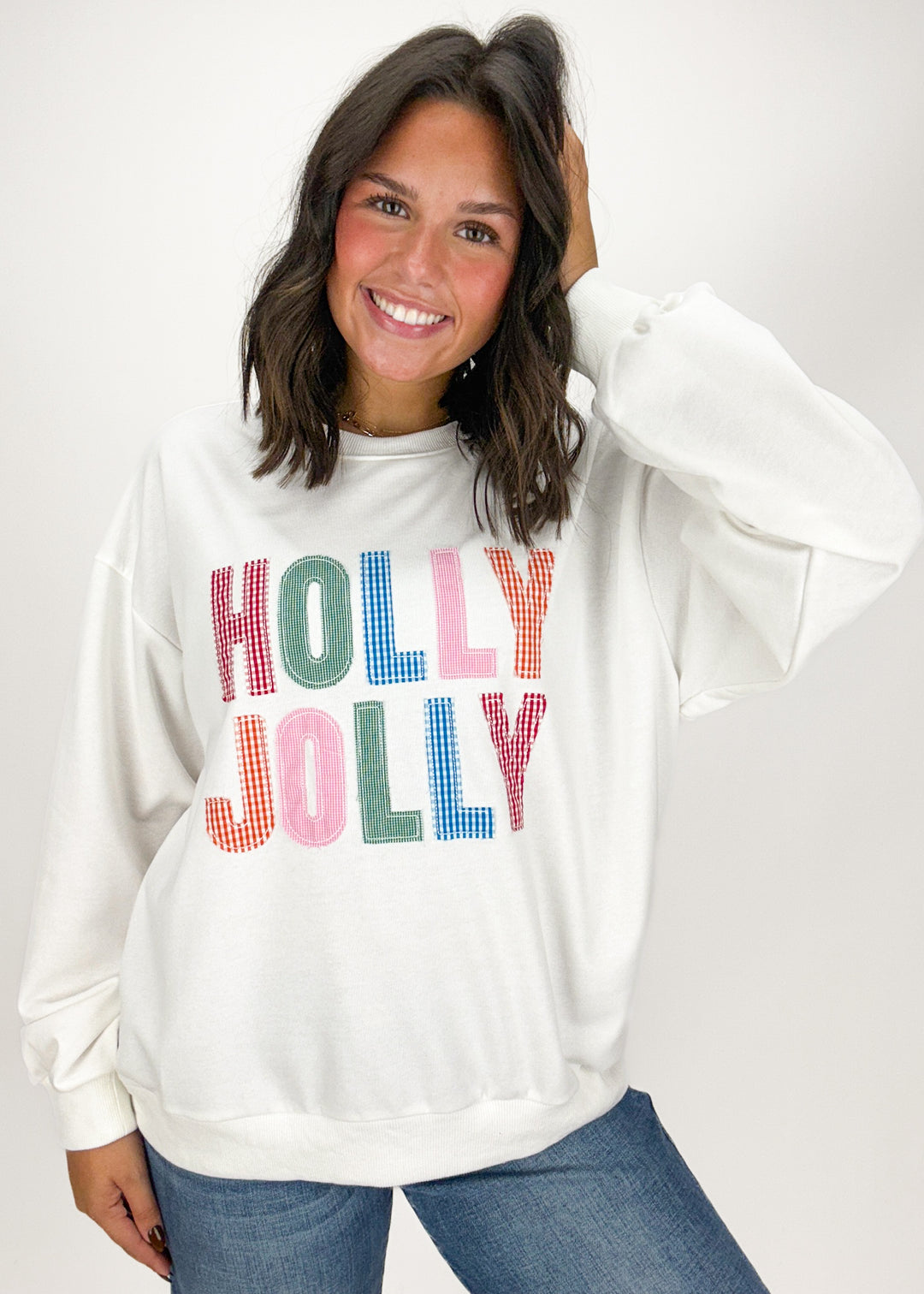 Woman wearing a white sweatshirt with 'Holly Jolly' text in colorful letters 