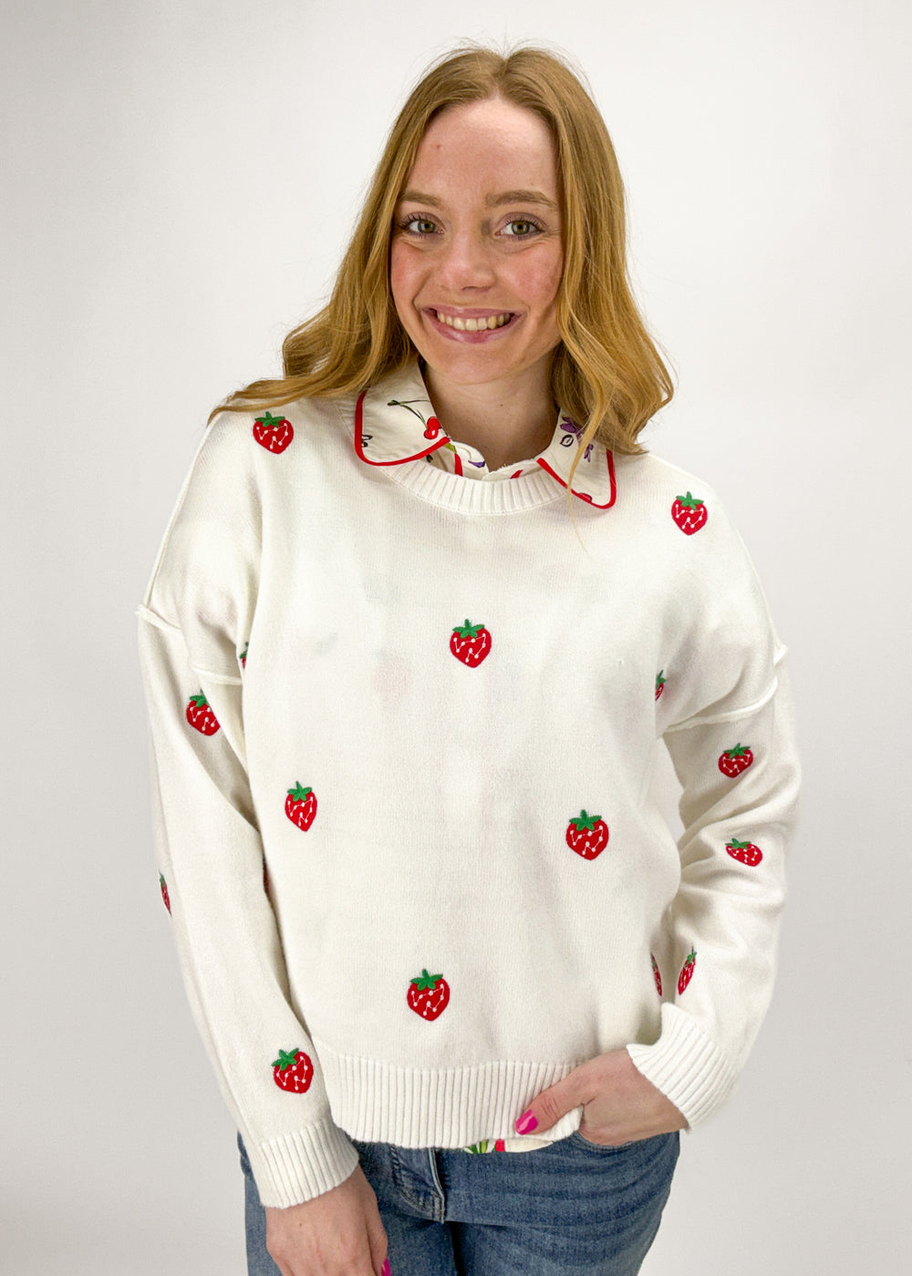 Woman wearing a white sweater with red strawberry patterns on a plain background