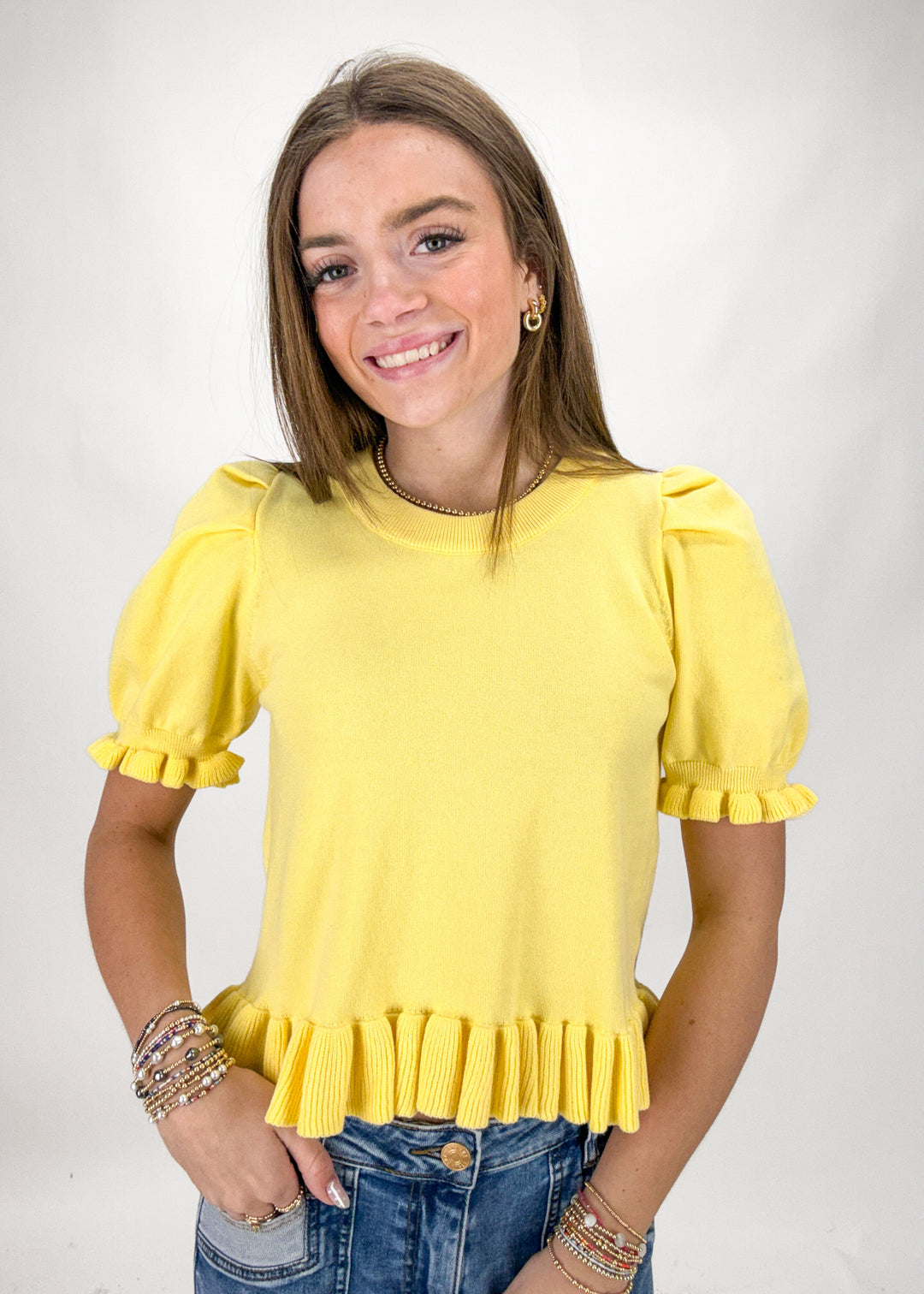 Woman wearing a yellow blouse with ruffled sleeves on a plain background